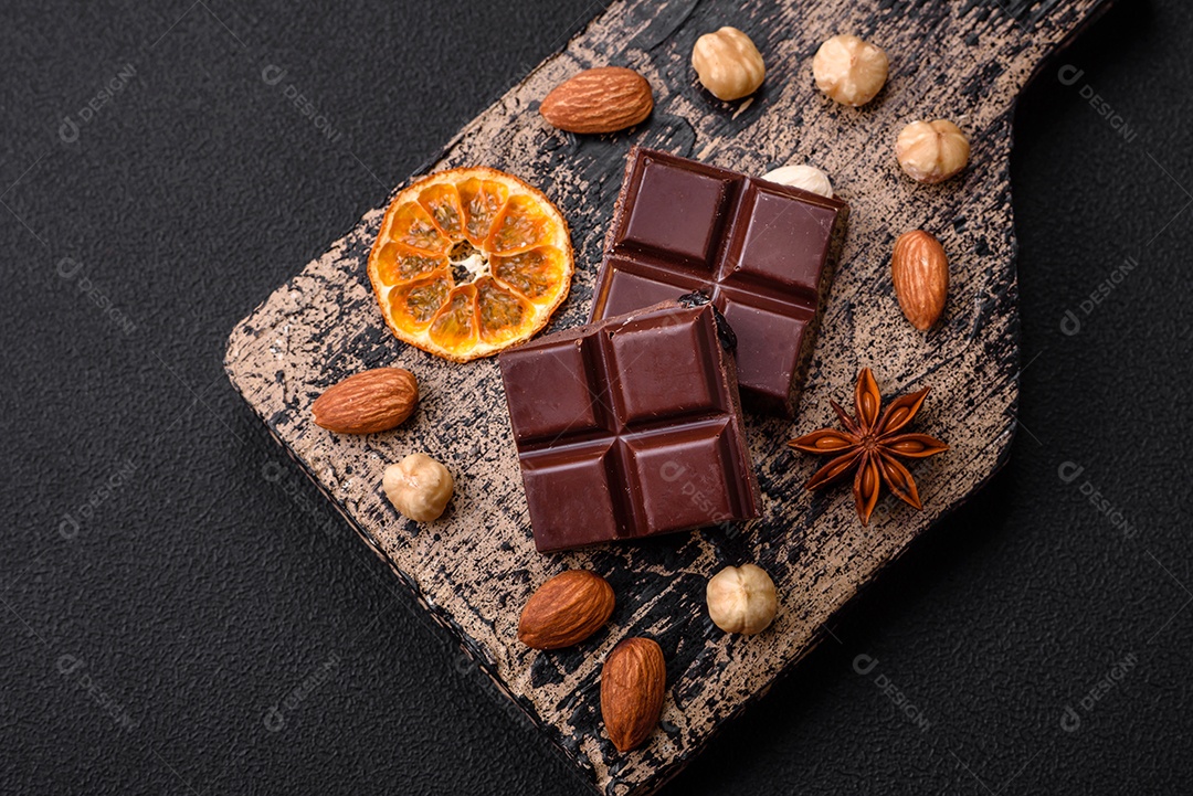 Delicioso chocolate preto doce quebrado em cubos em uma tábua de madeira sobre um fundo escuro de concreto