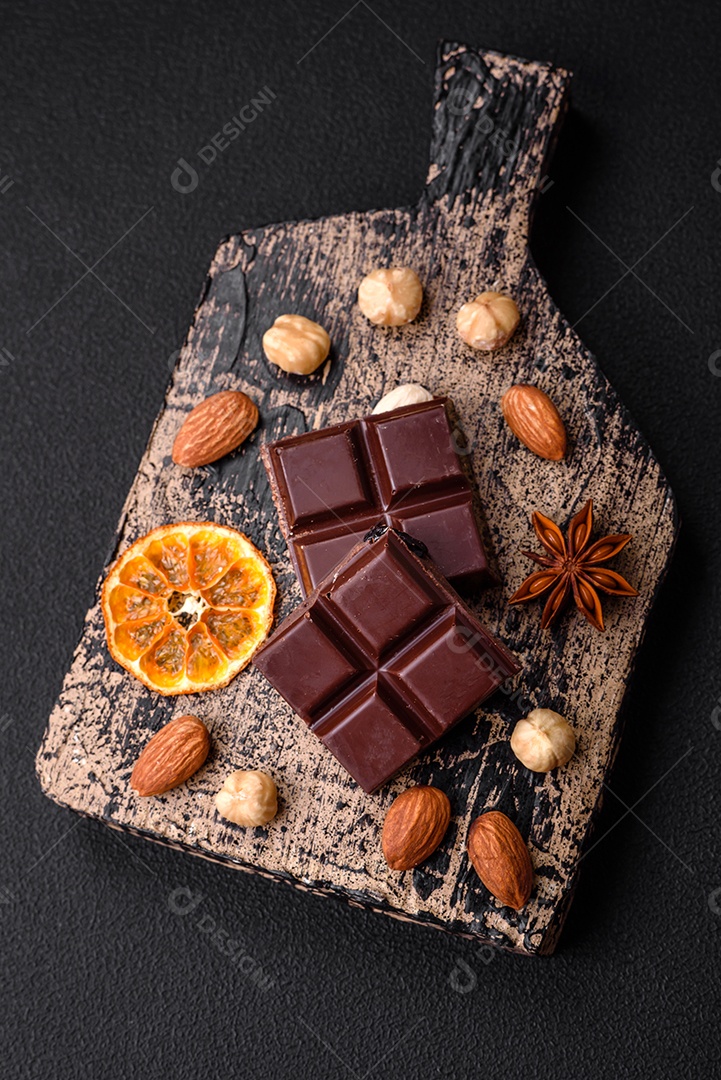 Delicioso chocolate preto doce quebrado em cubos em uma tábua de madeira sobre um fundo escuro de concreto