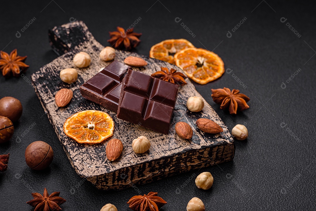 Delicioso chocolate preto doce quebrado em cubos em uma tábua de madeira sobre um fundo escuro de concreto