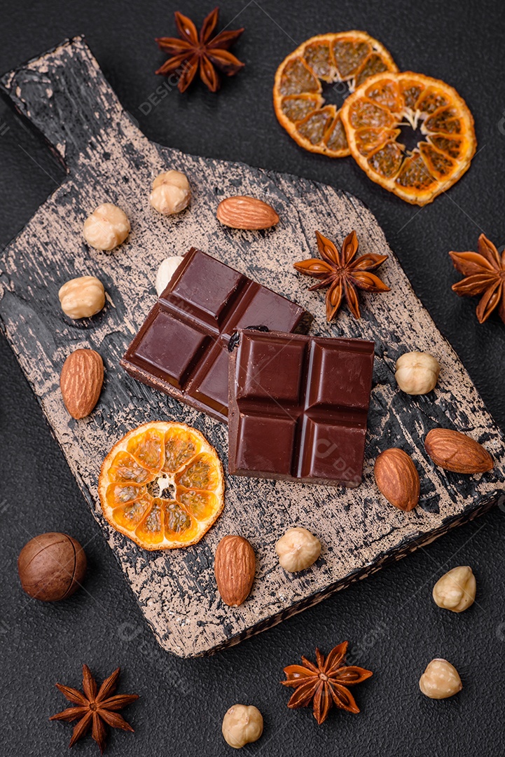 Delicioso chocolate preto doce quebrado em cubos em uma tábua de madeira sobre um fundo escuro de concreto