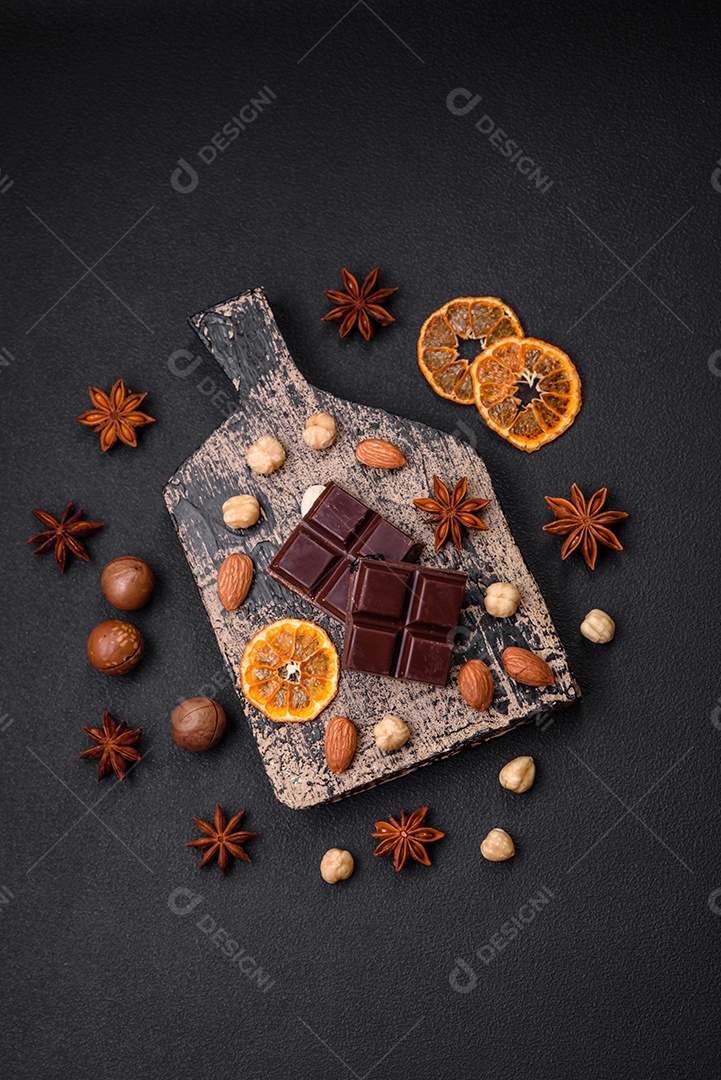 Delicioso chocolate preto doce quebrado em cubos em uma tábua de madeira sobre um fundo escuro de concreto