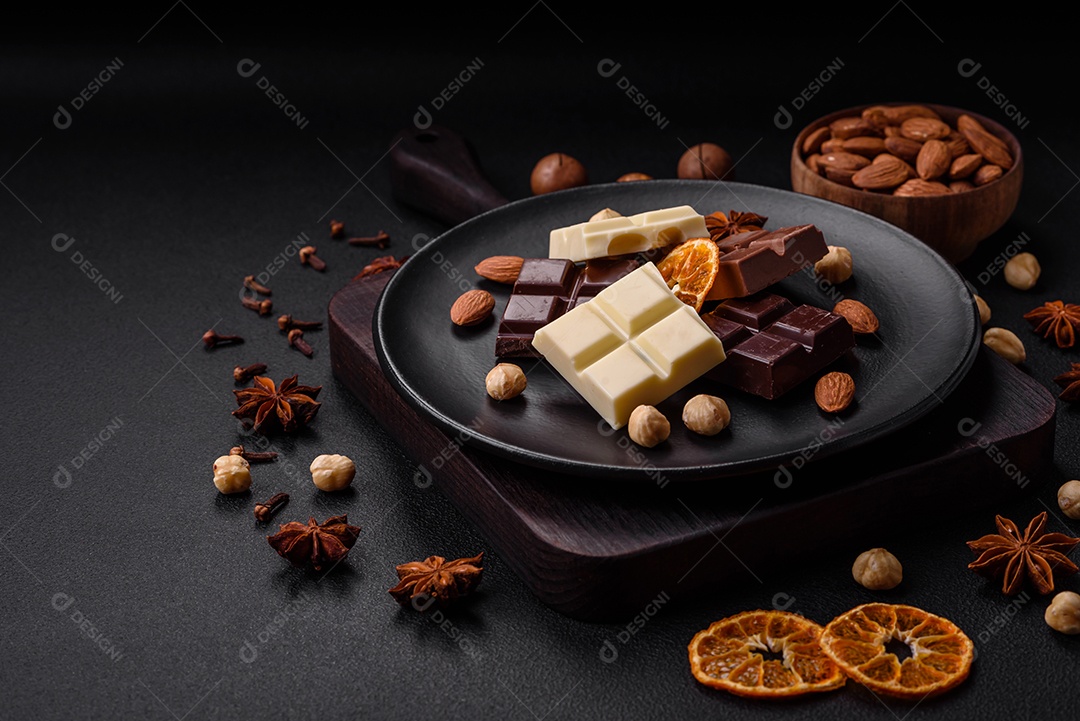 Uma mistura de vários tipos de delicioso chocolate doce quebrado em cubos em uma placa preta sobre fundo escuro de concreto