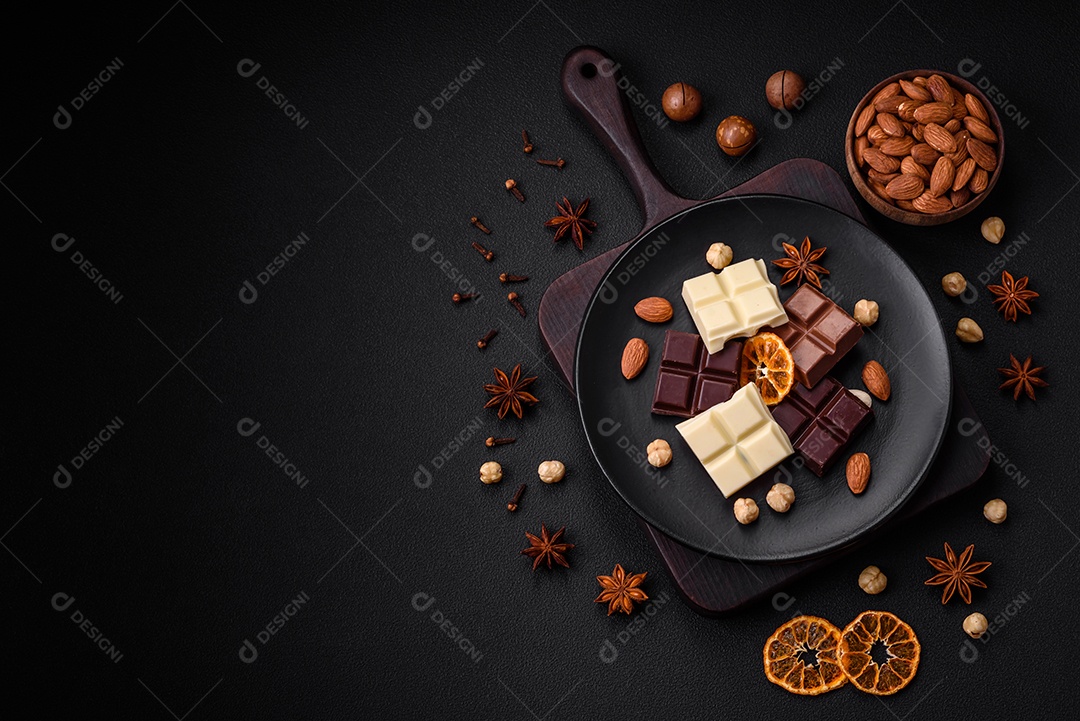 Uma mistura de vários tipos de delicioso chocolate doce quebrado em cubos em uma placa preta sobre fundo escuro de concreto