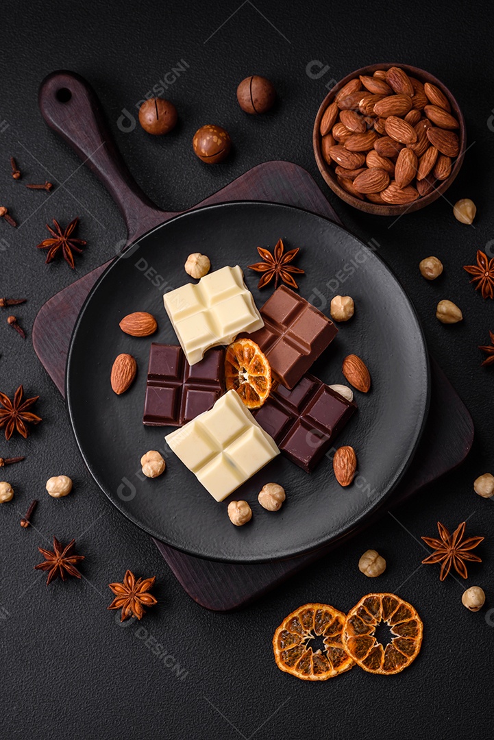 Uma mistura de vários tipos de delicioso chocolate doce quebrado em cubos em uma placa preta sobre fundo escuro de concreto