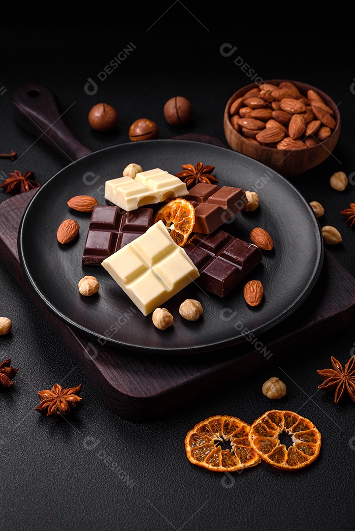 Uma mistura de vários tipos de delicioso chocolate doce quebrado em cubos em uma placa preta sobre fundo escuro de concreto