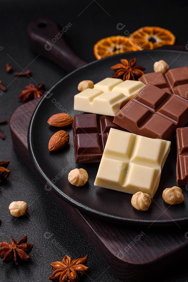 Uma mistura de vários tipos de delicioso chocolate doce quebrado em cubos em uma placa preta sobre fundo escuro de concreto