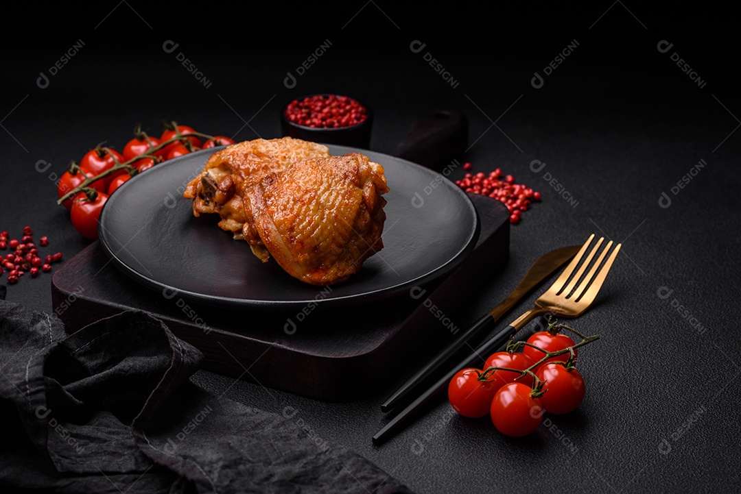 Deliciosas coxas de frango suculentas assadas com sal, especiarias e ervas em uma placa cerâmica sobre um fundo escuro de concreto