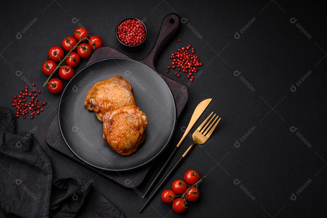 Deliciosas coxas de frango suculentas assadas com sal, especiarias e ervas em uma placa cerâmica sobre um fundo escuro de concreto
