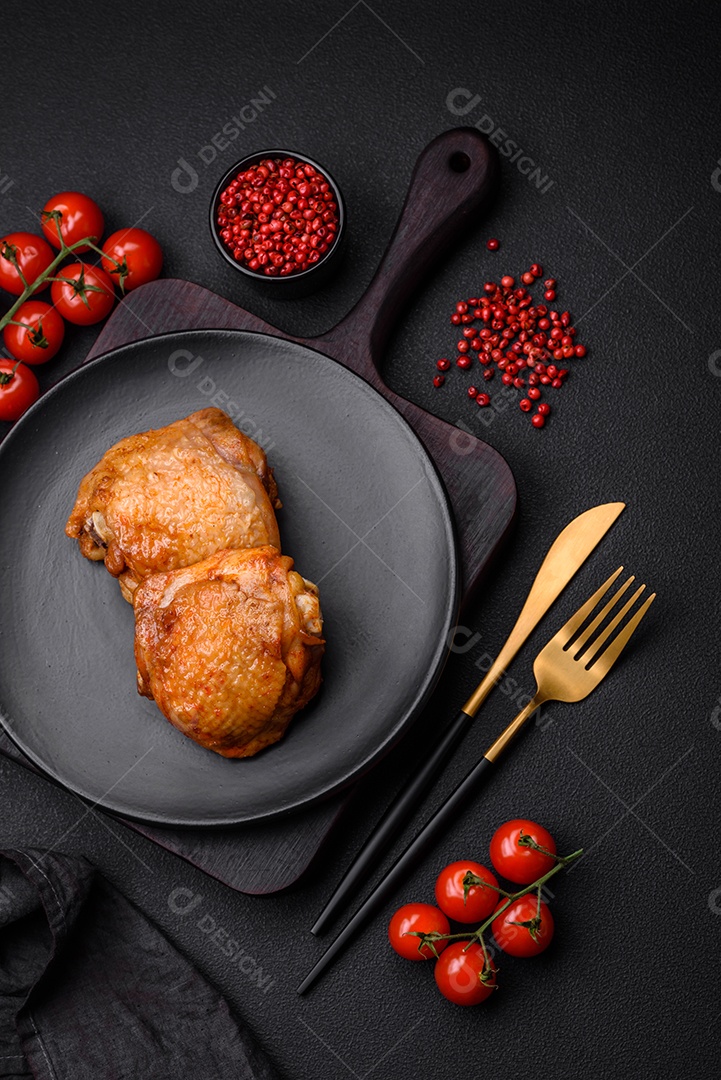 Deliciosas coxas de frango suculentas assadas com sal, especiarias e ervas em uma placa cerâmica sobre um fundo escuro de concreto