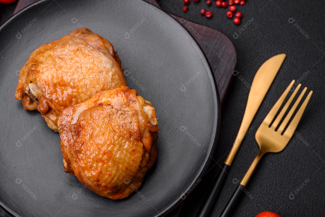 Deliciosas coxas de frango suculentas assadas com sal, especiarias e ervas em uma placa cerâmica sobre um fundo escuro de concreto
