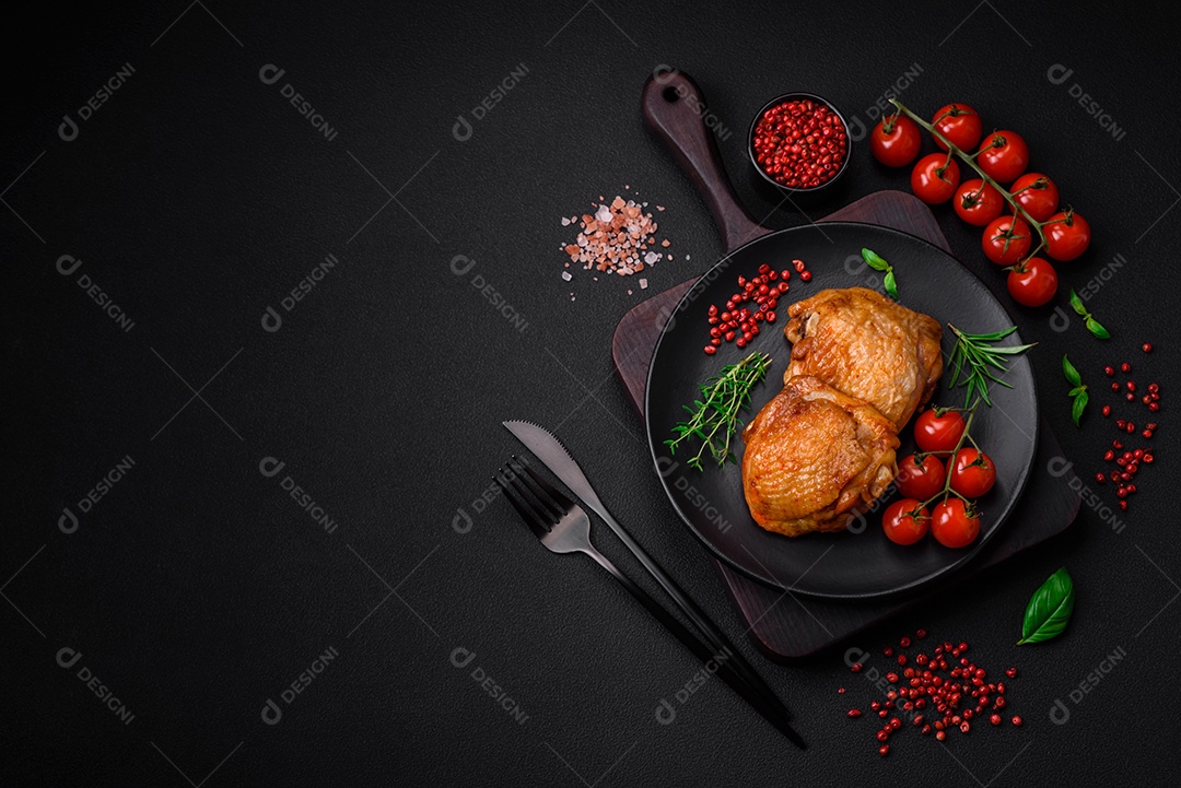 Deliciosas coxas de frango suculentas assadas com sal, especiarias e ervas em uma placa cerâmica sobre um fundo escuro de concreto