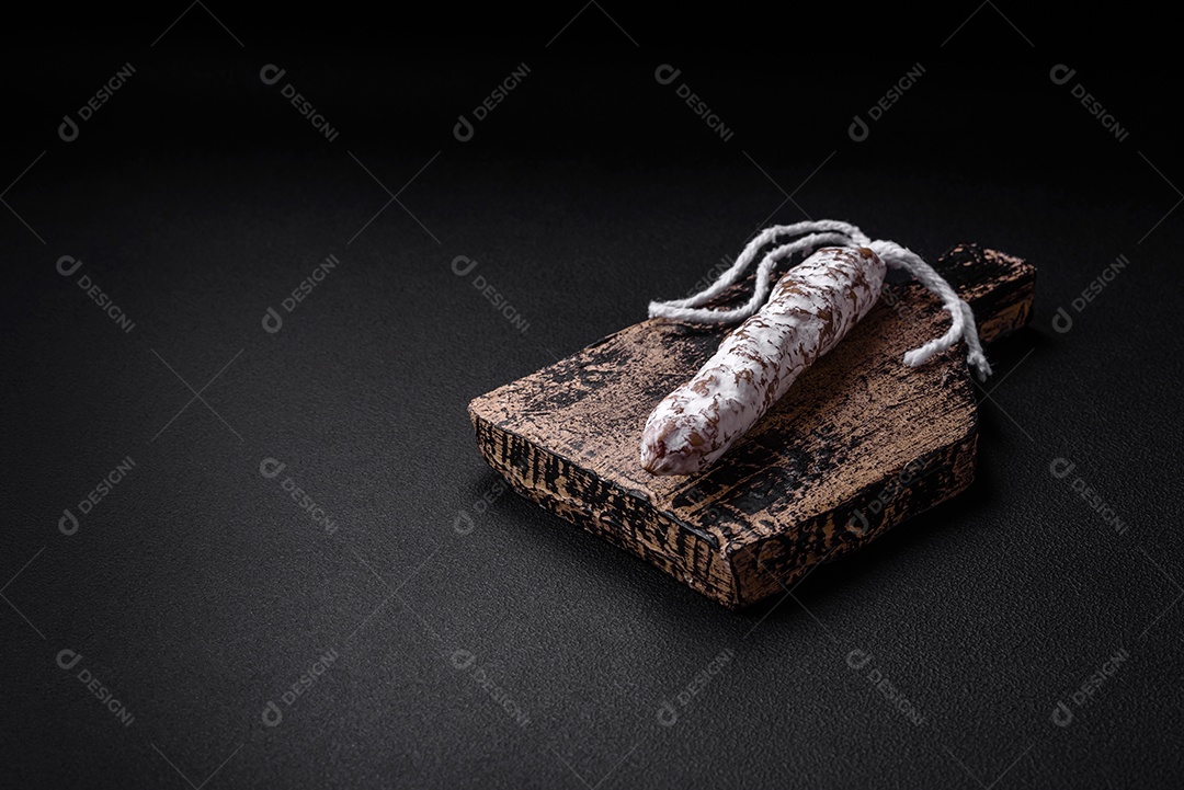 Deliciosa salsicha fuet fumada fresca com sal, especiarias e ervas sobre um fundo escuro de concreto