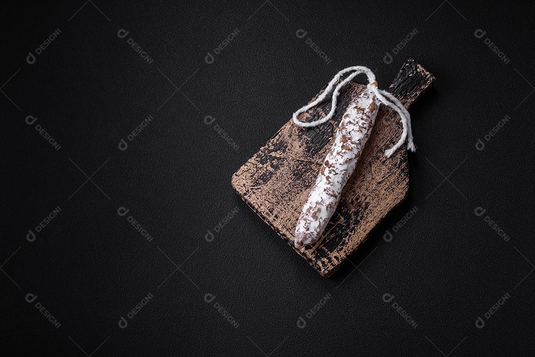 Deliciosa salsicha fuet fumada fresca com sal, especiarias e ervas sobre um fundo escuro de concreto