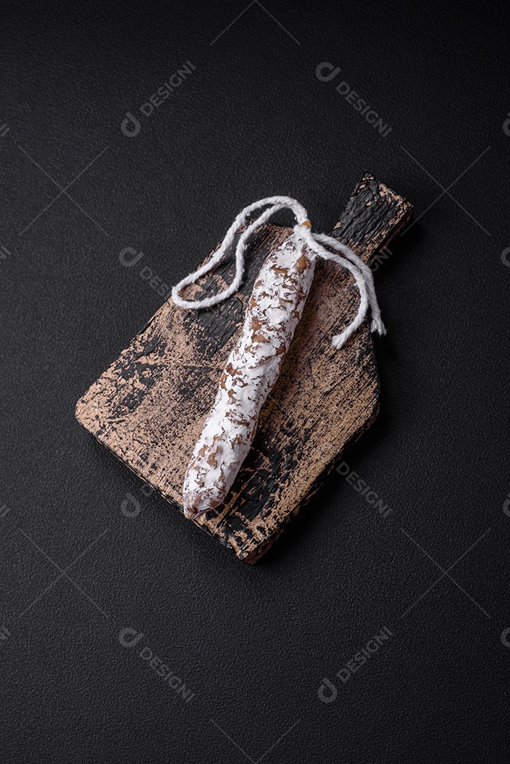 Deliciosa salsicha fuet fumada fresca com sal, especiarias e ervas sobre um fundo escuro de concreto