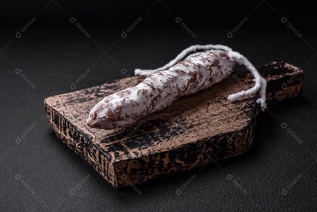 Deliciosa salsicha fuet fumada fresca com sal, especiarias e ervas sobre um fundo escuro de concreto