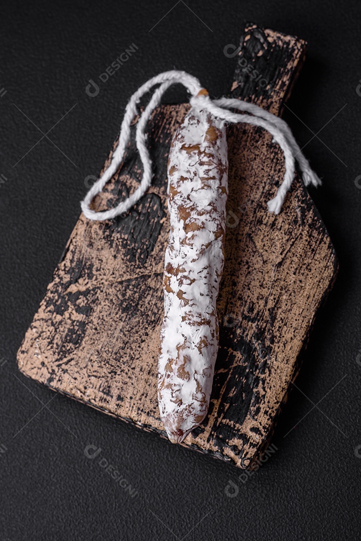 Deliciosa salsicha fuet fumada fresca com sal, especiarias e ervas sobre um fundo escuro de concreto