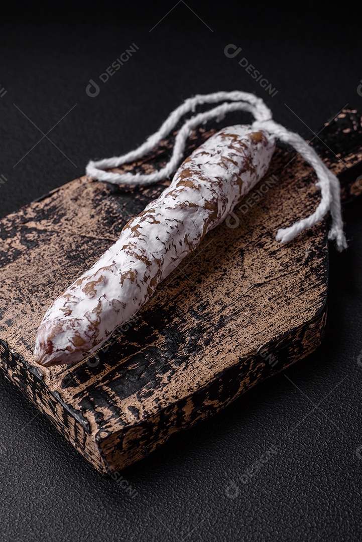 Deliciosa salsicha fuet fumada fresca com sal, especiarias e ervas sobre um fundo escuro de concreto