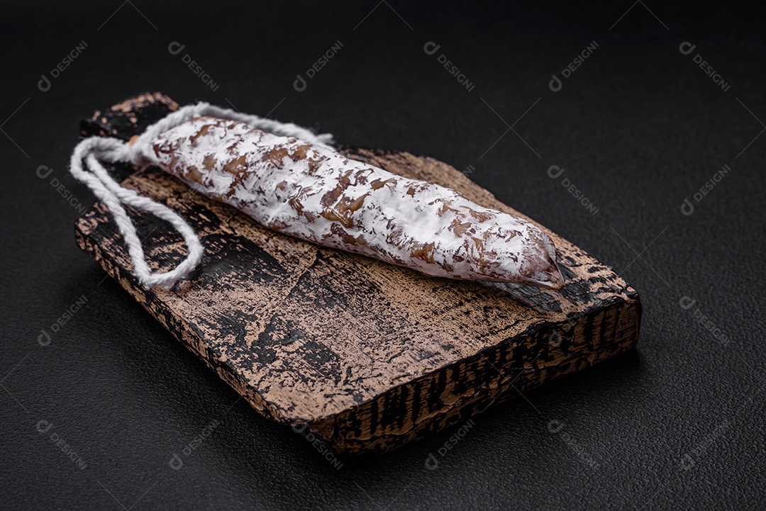 Deliciosa salsicha fuet fumada fresca com sal, especiarias e ervas sobre um fundo escuro de concreto