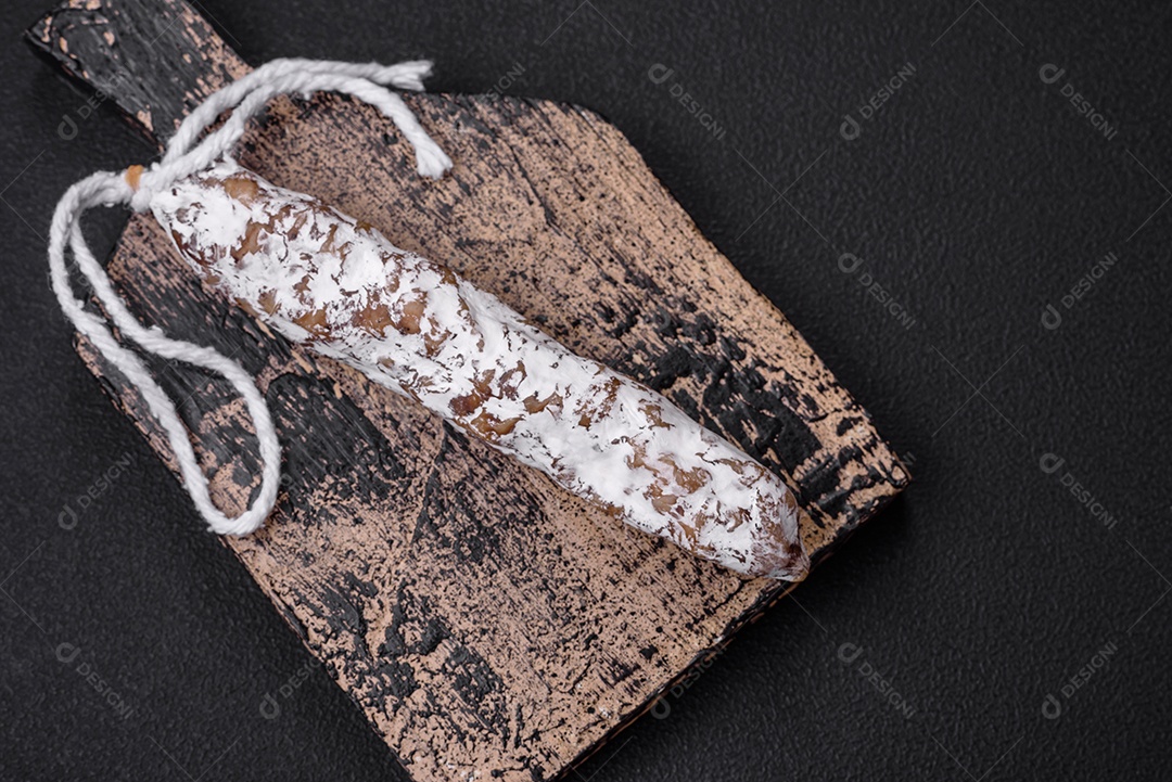 Deliciosa salsicha fuet fumada fresca com sal, especiarias e ervas sobre um fundo escuro de concreto