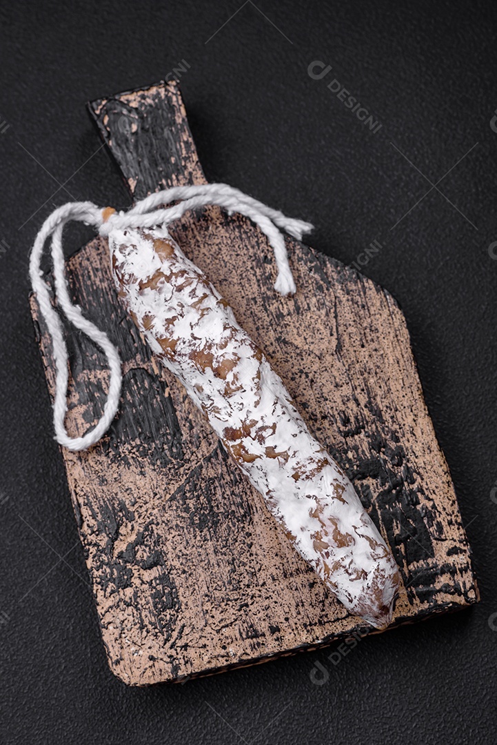 Deliciosa salsicha fuet fumada fresca com sal, especiarias e ervas sobre um fundo escuro de concreto