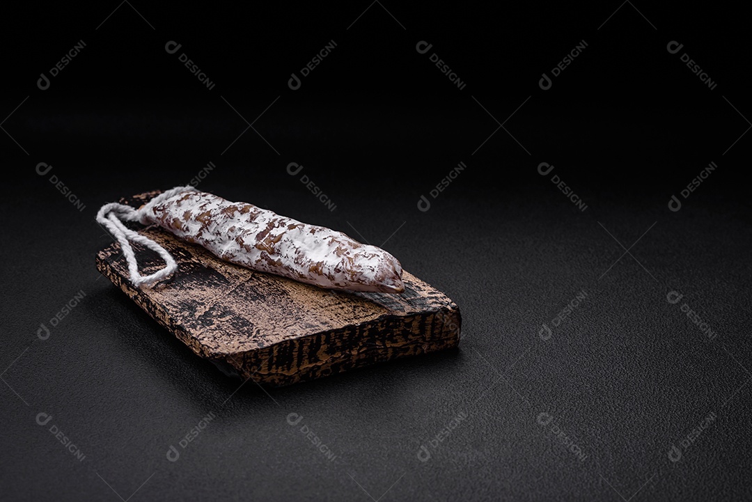 Deliciosa salsicha fuet fumada fresca com sal, especiarias e ervas sobre um fundo escuro de concreto