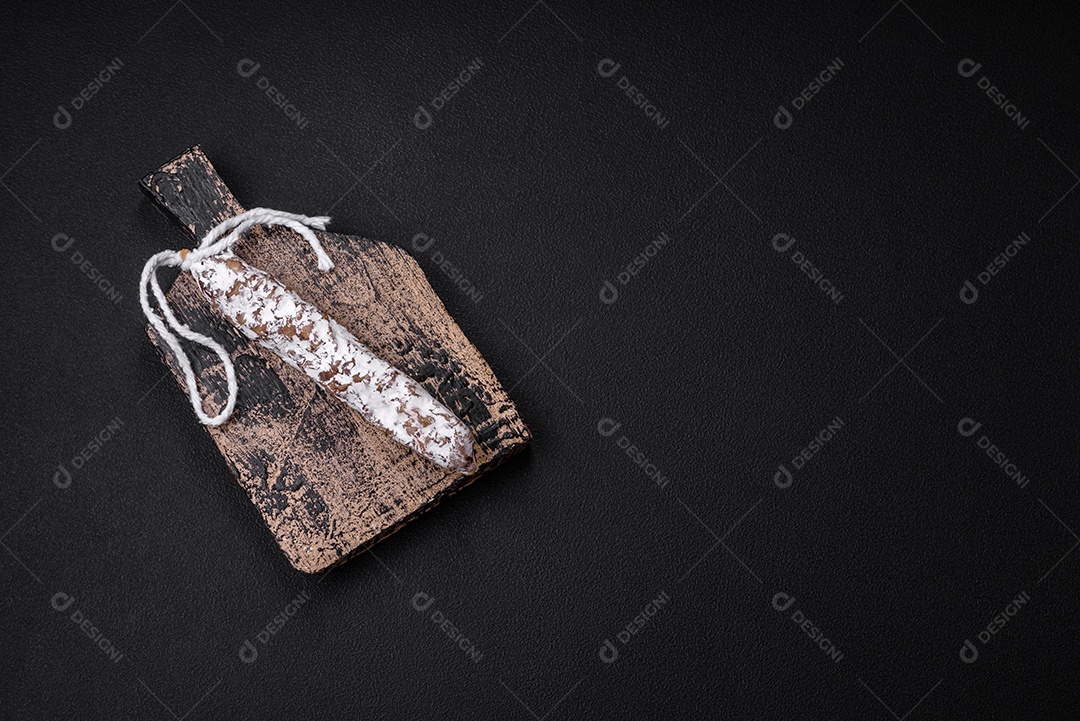 Deliciosa salsicha fuet fumada fresca com sal, especiarias e ervas sobre um fundo escuro de concreto