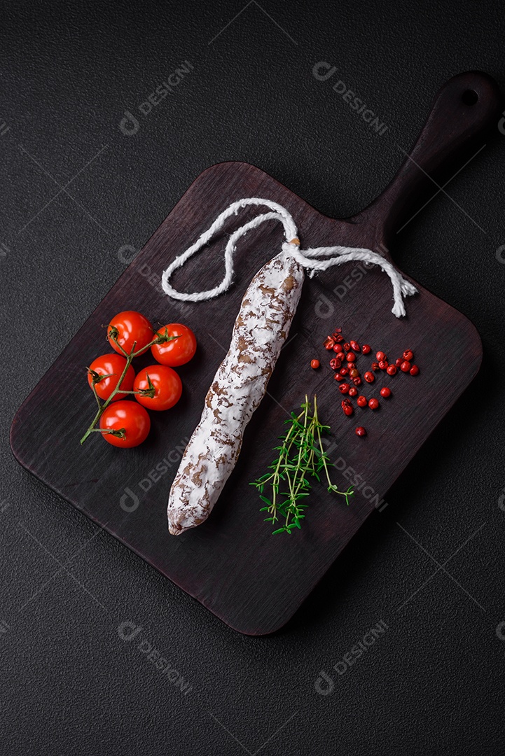 Deliciosa salsicha fuet fumada fresca com sal, especiarias e ervas sobre um fundo escuro de concreto