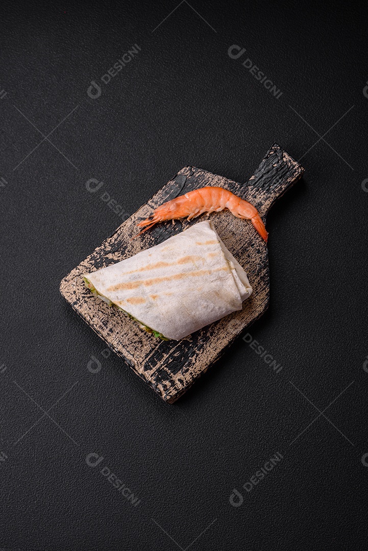 Delicioso pão fresco com camarões, tomates, alface e pepino em pão pita sobre um fundo escuro de concreto