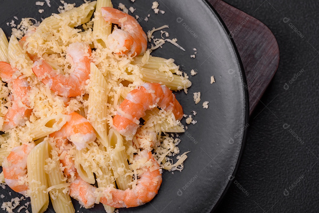 Deliciosa massa penna fresca com camarão, molho, queijo, sal e especiarias sobre um fundo escuro de concreto