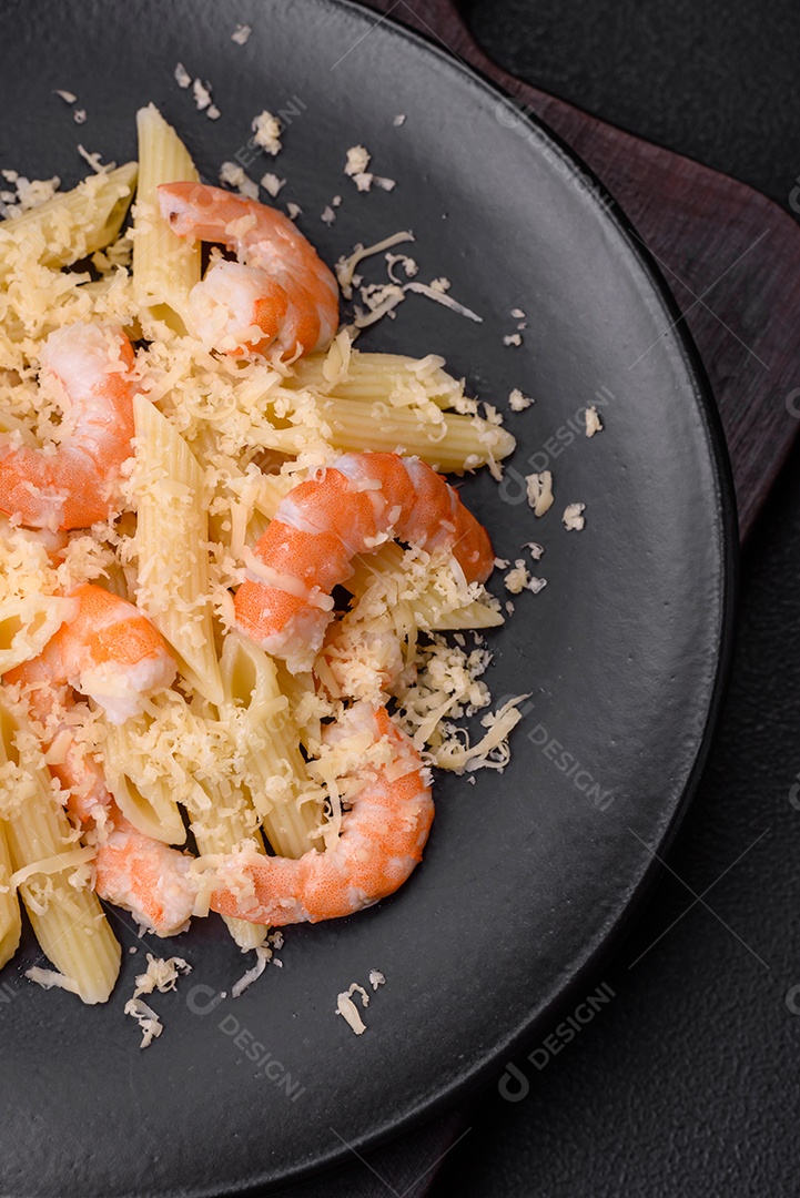 Deliciosa massa penna fresca com camarão, molho, queijo, sal e especiarias sobre um fundo escuro de concreto