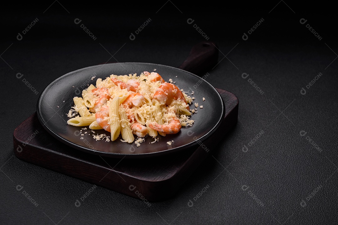 Deliciosa massa penna fresca com camarão, molho, queijo, sal e especiarias sobre um fundo escuro de concreto