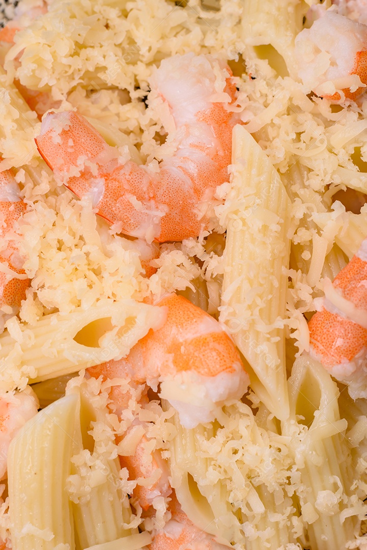 Deliciosa massa penna fresca com camarão, molho, queijo, sal e especiarias sobre um fundo escuro de concreto