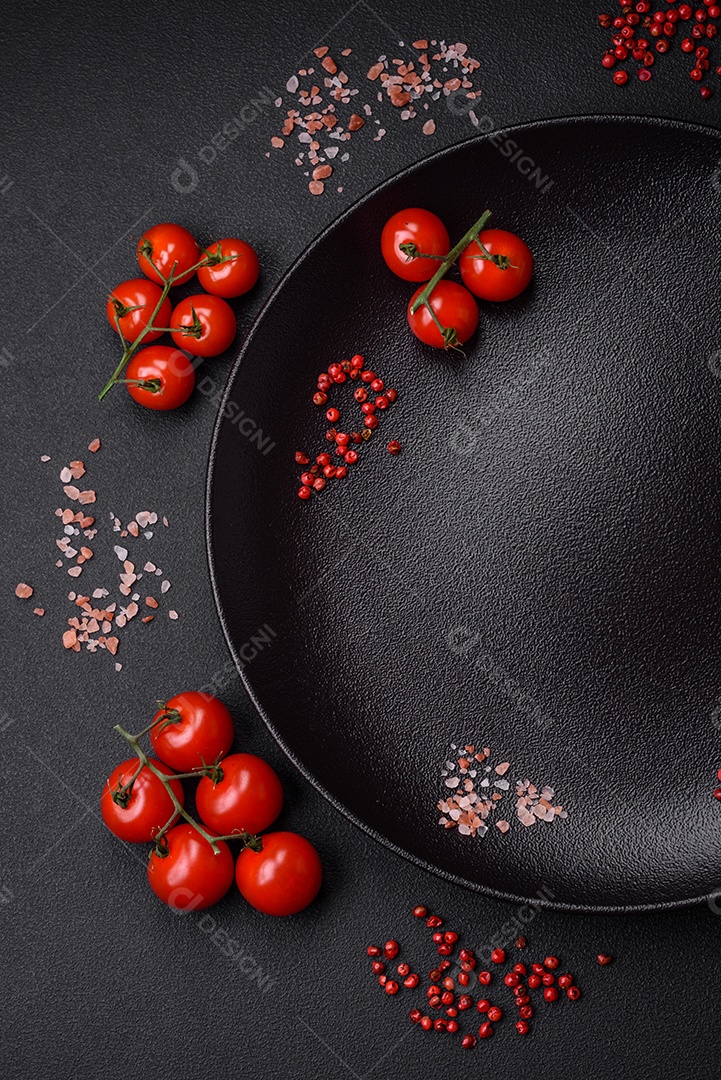 Ingredientes para cozinhar tomate cereja, sal, especiarias e ervas sobre um fundo escuro de concreto