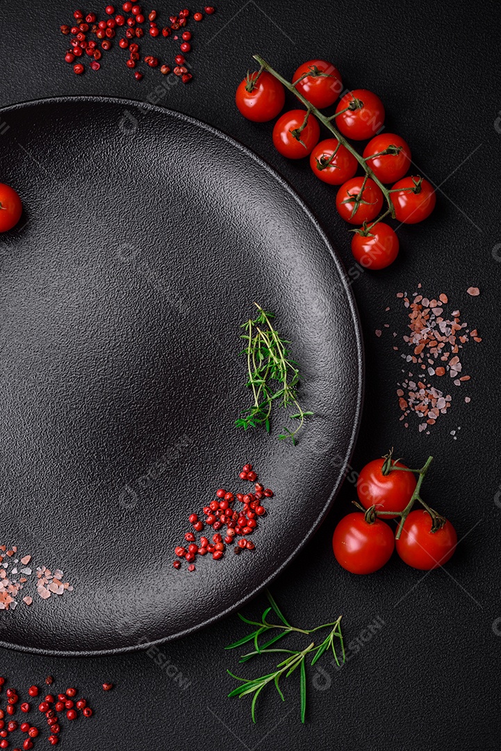 Ingredientes para cozinhar tomate cereja, sal, especiarias e ervas sobre um fundo escuro de concreto