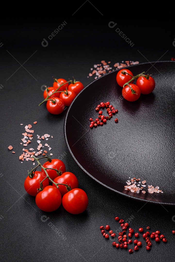 Ingredientes para cozinhar tomate cereja, sal, especiarias e ervas sobre um fundo escuro de concreto