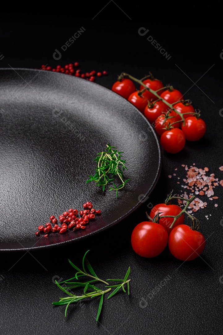 Ingredientes para cozinhar tomate cereja, sal, especiarias e ervas sobre um fundo escuro de concreto