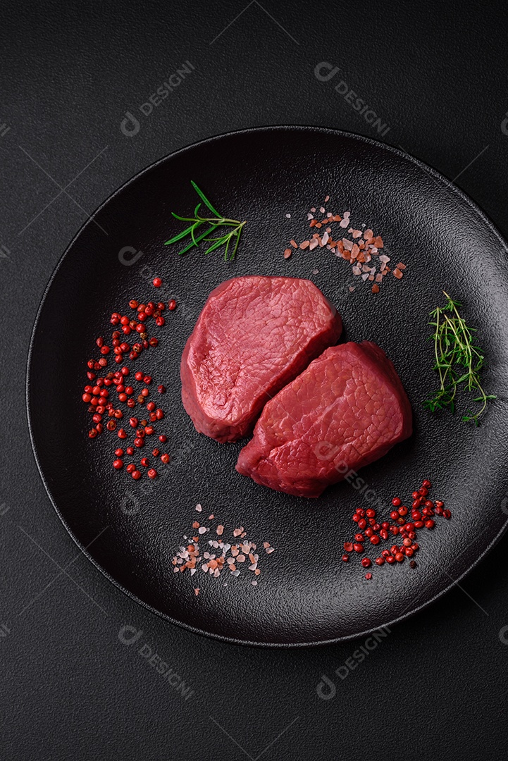 Bife cru redondo com sal, especiarias e ervas preparadas para grelhar em um fundo texturizado