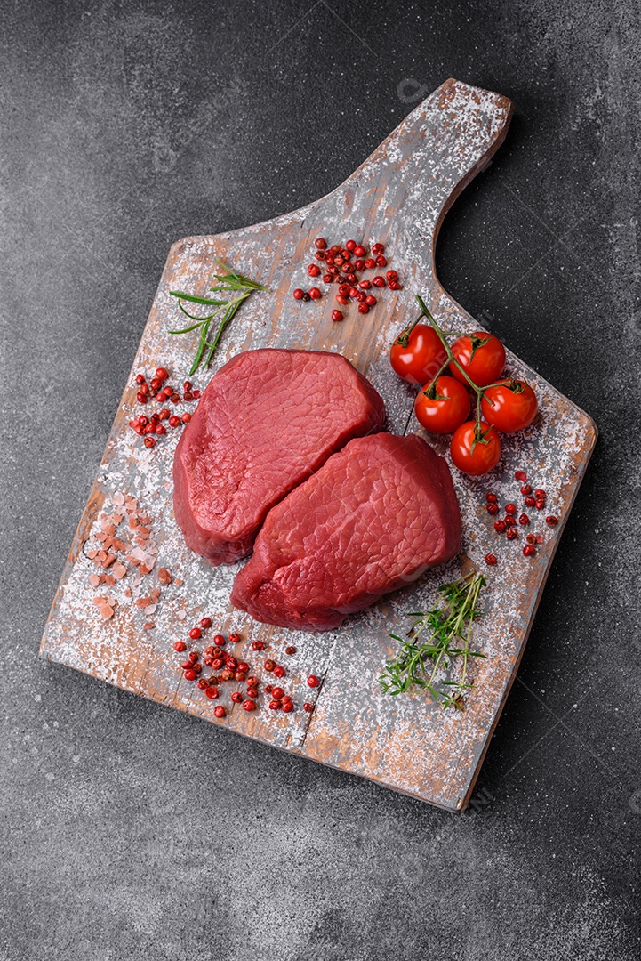 Bife cru redondo com sal, especiarias e ervas preparadas para grelhar em um fundo texturizado