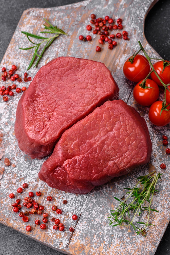 Bife cru redondo com sal, especiarias e ervas preparadas para grelhar em um fundo texturizado