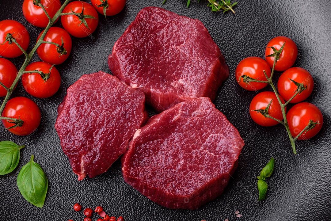 Carne crua suculenta com especiarias, sal e ervas sobre um fundo escuro de concreto. Preparando-se para cozinhar um prato de carne