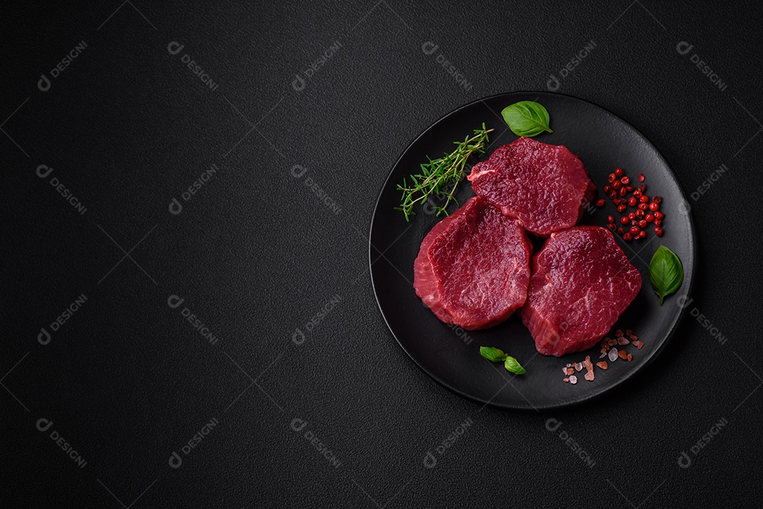 Carne crua suculenta com especiarias, sal e ervas sobre um fundo escuro de concreto. Preparando-se para cozinhar um prato de carne