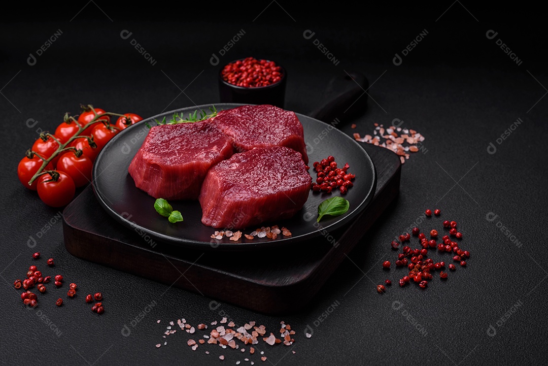 Carne crua suculenta com especiarias, sal e ervas sobre um fundo escuro de concreto. Preparando-se para cozinhar um prato de carne