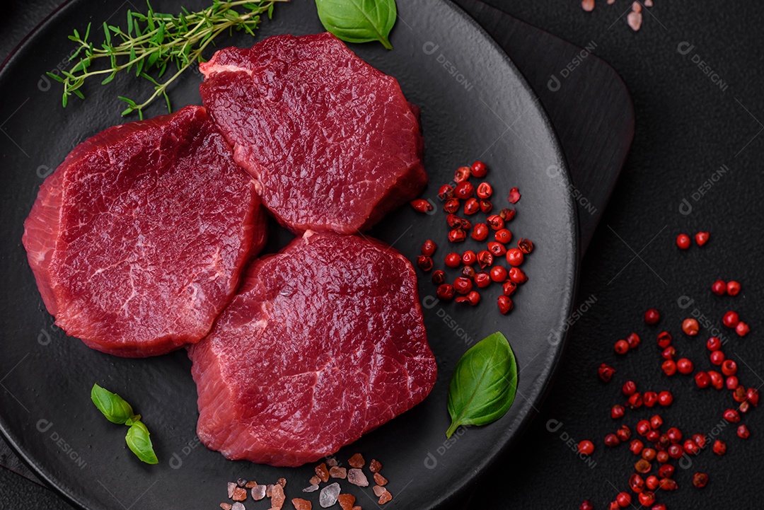 Carne crua suculenta com especiarias, sal e ervas sobre um fundo escuro de concreto. Preparando-se para cozinhar um prato de carne