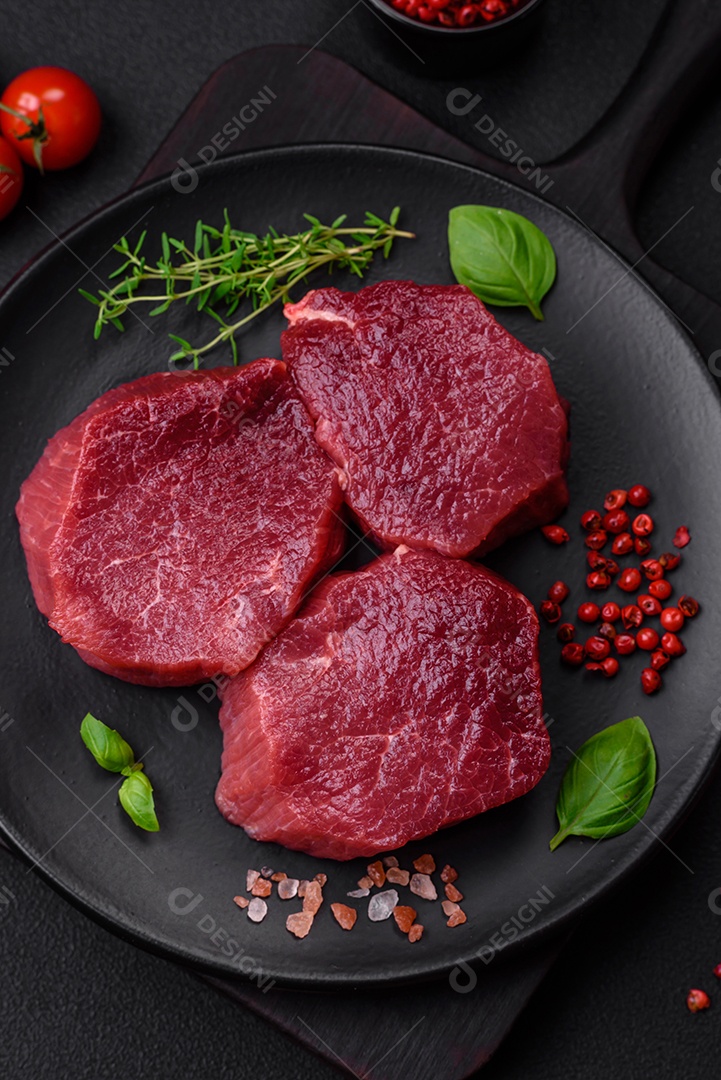 Carne crua suculenta com especiarias, sal e ervas sobre um fundo escuro de concreto. Preparando-se para cozinhar um prato de carne