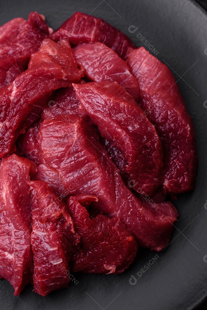 Carne crua suculenta com especiarias, sal e ervas sobre um fundo escuro de concreto. Preparando-se para cozinhar um prato de carne