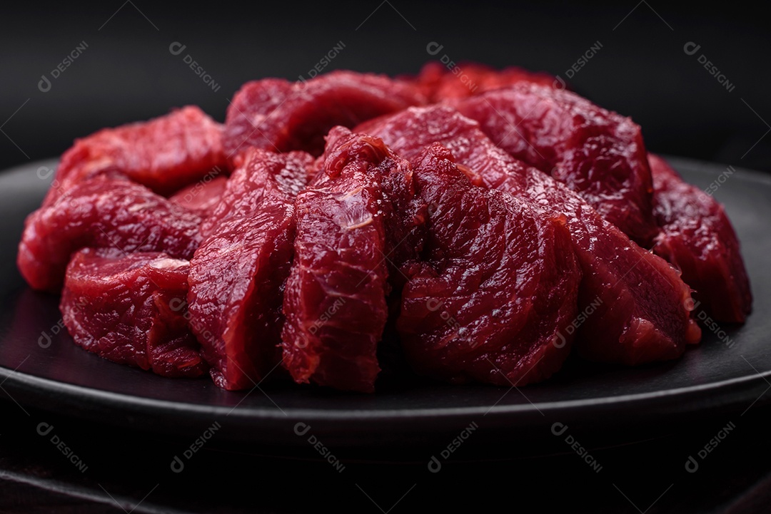 Carne crua suculenta com especiarias, sal e ervas sobre um fundo escuro de concreto. Preparando-se para cozinhar um prato de carne