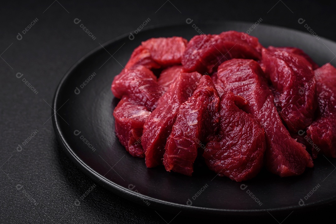 Carne crua suculenta com especiarias, sal e ervas sobre um fundo escuro de concreto. Preparando-se para cozinhar um prato de carne