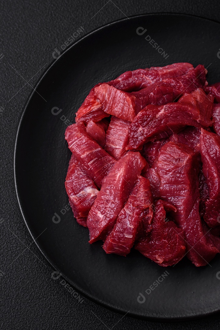 Carne crua suculenta com especiarias, sal e ervas sobre um fundo escuro de concreto. Preparando-se para cozinhar um prato de carne