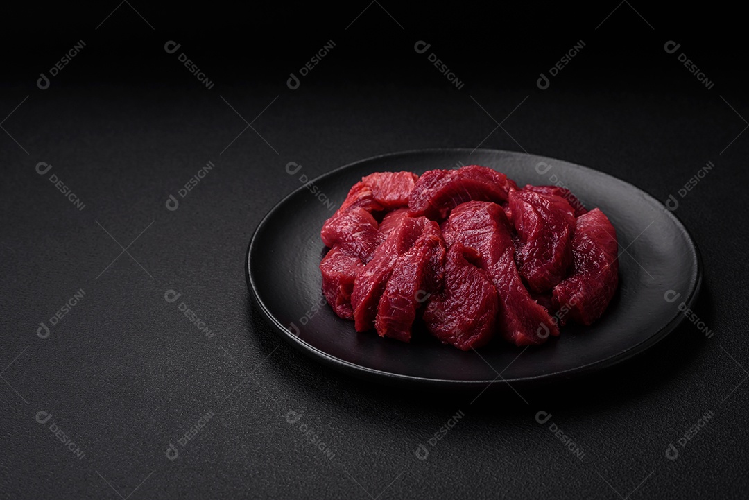 Carne crua suculenta com especiarias, sal e ervas sobre um fundo escuro de concreto. Preparando-se para cozinhar um prato de carne