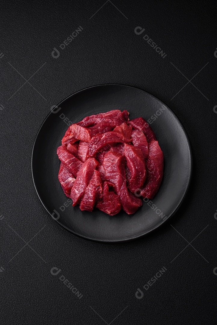 Carne crua suculenta com especiarias, sal e ervas sobre um fundo escuro de concreto. Preparando-se para cozinhar um prato de carne